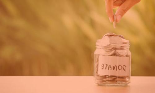 一只手把钱放进一个罐子里，上面写着“捐赠”.